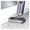 A cordless floor cleaner is shown cleaning debris from a tiled floor near a white baseboard. Produktbild-Vorschau