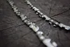 Two chainsaw chains are laid diagonally across a dark, textured wooden surface, likely a tree stump. Náhled obrázku produktu