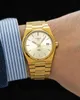 A close-up shot of a gold Tissot PRX watch on a person's wrist, with a blue and white striped shirt cuff visible. Anteprima dell’immagine prodotto
