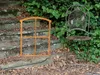 A rustic metal window frame and a vintage chair are placed on stone steps outdoors, surrounded by greenery and fallen leaves. Produktbild-Vorschau