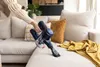 A person is using a cordless vacuum cleaner to clean a sofa. Náhľad obrázku produktu