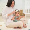 A mother is brushing her baby's hair while sitting on a rug. Produktbild-Vorschau