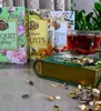 A collection of tea boxes and a glass of tea are arranged on a reflective surface, with loose tea leaves scattered around. Produktbild-Vorschau