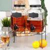 Two beverage dispensers with spigots on a black metal stand, with a glass of beverage and fruit in the foreground. Náhľad obrázku produktu