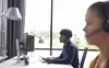 Two people wearing headsets are working at computers in an office setting. Náhled obrázku produktu
