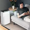 A man with headphones is relaxing on a couch while a portable air conditioner operates nearby. Anteprima dell’immagine prodotto