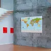 A world map poster is displayed on a concrete wall in a modern room with wooden stairs and red wall art. Produktbild-Vorschau