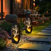 Two solar-powered garden lights with a tree design illuminate a pathway at dusk. Produktbild-Vorschau