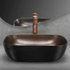 A modern bathroom sink with a copper faucet, set against a textured concrete wall and a reflective mirror. Anteprima dell’immagine prodotto