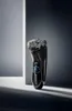 A black electric shaver with blue accents is displayed against a gradient gray background with dramatic lighting. Voir les images du produit
