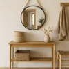 A round mirror hangs above a wooden console table with decorative items. Produktbild-Vorschau