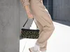 A person is holding a small leopard-print pouch bag while leaning against a concrete wall. Produktbild-Vorschau