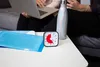 A close-up of a desk with a timer, a blue folder, and a water bottle, with people working on a laptop in the background. Produktbild-Vorschau
