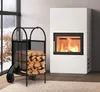 A modern white fireplace with a roaring fire, next to a black metal log holder filled with firewood. A large window with a snowy landscape is visible in the background. Podgląd zdjęcia produktu