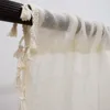 A close-up view of a cream-colored sheer curtain with tassels hanging from a dark curtain rod. Produktbild-Vorschau