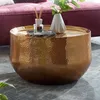 A gold hammered coffee table with decorative items on top, placed in a living room setting.