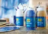 A collection of acrylic paint bottles and art supplies on a wooden surface. Anteprima dell’immagine prodotto