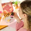A woman is holding a small bottle of liquid in front of an open box of similar bottles. Produktbild-Vorschau