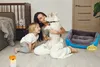 A woman and a child are playing with a dog in a room, with a dog bed in the foreground. Podgląd zdjęcia produktu