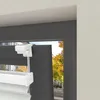 Close-up of a white blind mechanism attached to a dark window frame, with trees and a street visible through the window. Produktbild-Vorschau