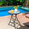A small round glass-top table with a metal frame is set up next to a swimming pool, with a vase of flowers and a drink on it. Anteprima dell’immagine prodotto