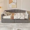 A gray upholstered daybed with storage drawers is shown in a bedroom setting with a piece of abstract art on the wall. Produktbild-Vorschau