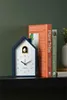 A dark blue cuckoo clock sits on a shelf next to two books. Anteprima dell’immagine prodotto