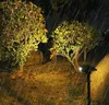 A solar-powered garden light illuminates a bush and the surrounding ground during a rain shower at night. Anteprima dell’immagine prodotto