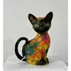 A colorful, mosaic-style cat figurine with a white cord plugged into its base, sitting on a white surface against a white background. Produktbild-Vorschau