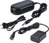 A black camera battery charger and dummy battery adapter kit is laid out on a white background. Náhled obrázku produktu