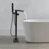 A black freestanding bathtub faucet with a handheld showerhead is filling a white bathtub. Podgląd zdjęcia produktu