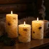 Three LED candles with a birch wood effect are arranged on a wooden surface, with a mug of steaming coffee and pine cones in the background. Produktbild-Vorschau