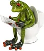 A ceramic frog figurine sitting on a toilet and reading a newspaper. Produktbild-Vorschau