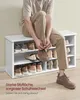 A person is sitting on a shoe bench and putting on a shoe. The shoe bench is filled with shoes. Produktbild-Vorschau