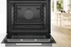 An open built-in oven with a clean interior, set in a modern kitchen environment with a dining table and chairs visible in the background. Produktbild-Vorschau