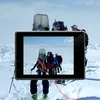 A group of people are hiking in a snowy, mountainous environment. A camera is positioned in the foreground, displaying a view of the hikers. Anteprima dell’immagine prodotto