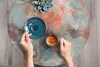 A person's hands are holding a cup of coffee and a spoon over a marble-patterned table. Náhľad obrázku produktu