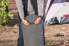 A person is shown adjusting a buckle on a rolled-up air mattress outdoors, with a tent in the background. Podgląd zdjęcia produktu
