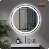 A round LED mirror is mounted on a gray wall above a bathroom vanity. The mirror reflects a shower stall and plants. The vanity has a soap dispenser and a faucet. Podgląd zdjęcia produktu