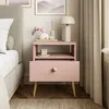 A pink nightstand next to a bed, decorated with a lamp, vase, and candle. Náhled obrázku produktu