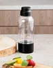 A clear plastic bottle with a black base and cap sits on a countertop, with fruit slices and cinnamon sticks in the foreground. Produktbild-Vorschau