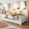 A bedroom scene featuring a white daybed with a tufted beige headboard, a pull-out trundle bed, and a built-in shelf unit with LED lighting. Produktbild-Vorschau