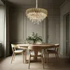 A dining room with a round wooden table and chairs, illuminated by a gold and crystal chandelier. Produktbild-Vorschau