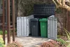 A storage unit for trash cans is shown outdoors, next to a building and surrounded by plants. Náhled obrázku produktu