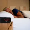 A man sleeping in bed with a digital alarm clock on the nightstand. Produktbild-Vorschau