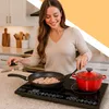A woman is cooking on a black induction cooktop in a kitchen. Voir les images du produit