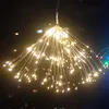 A string of warm white LED lights resembling a firework burst, hanging in a dark environment with blurred lights in the background. Produktbild-Vorschau
