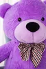 Close-up of a large purple teddy bear's face and chest, wearing a checkered bow tie. Voir les images du produit