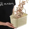 A person wearing a black t-shirt with a logo is holding a beige laundry basket filled with wooden clothespins. Podgląd zdjęcia produktu