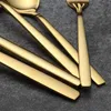 A close-up view of several gold-colored cutlery pieces, including spoons and forks, laid out on a gray surface. Anteprima dell’immagine prodotto